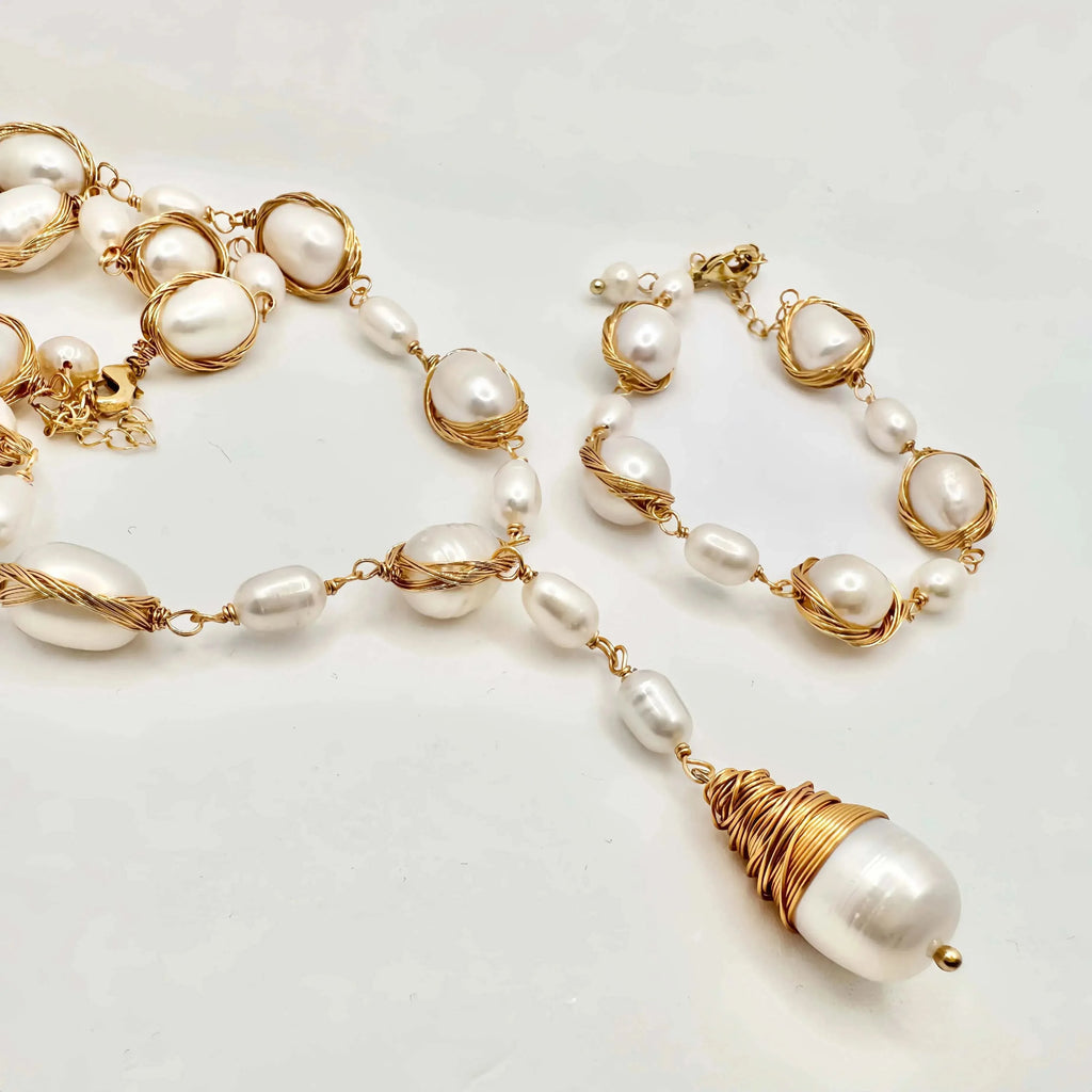 A luxurious pearl jewelry set on a white surface, consisting of a necklace and bracelet. Both pieces feature large, lustrous pearls encased in twisted gold wire, interspersed with smaller pearls linked by gold chains. The necklace is highlighted by a large, baroque pearl pendant, wrapped in a dense coil of gold wire, adding a striking visual element to the set.