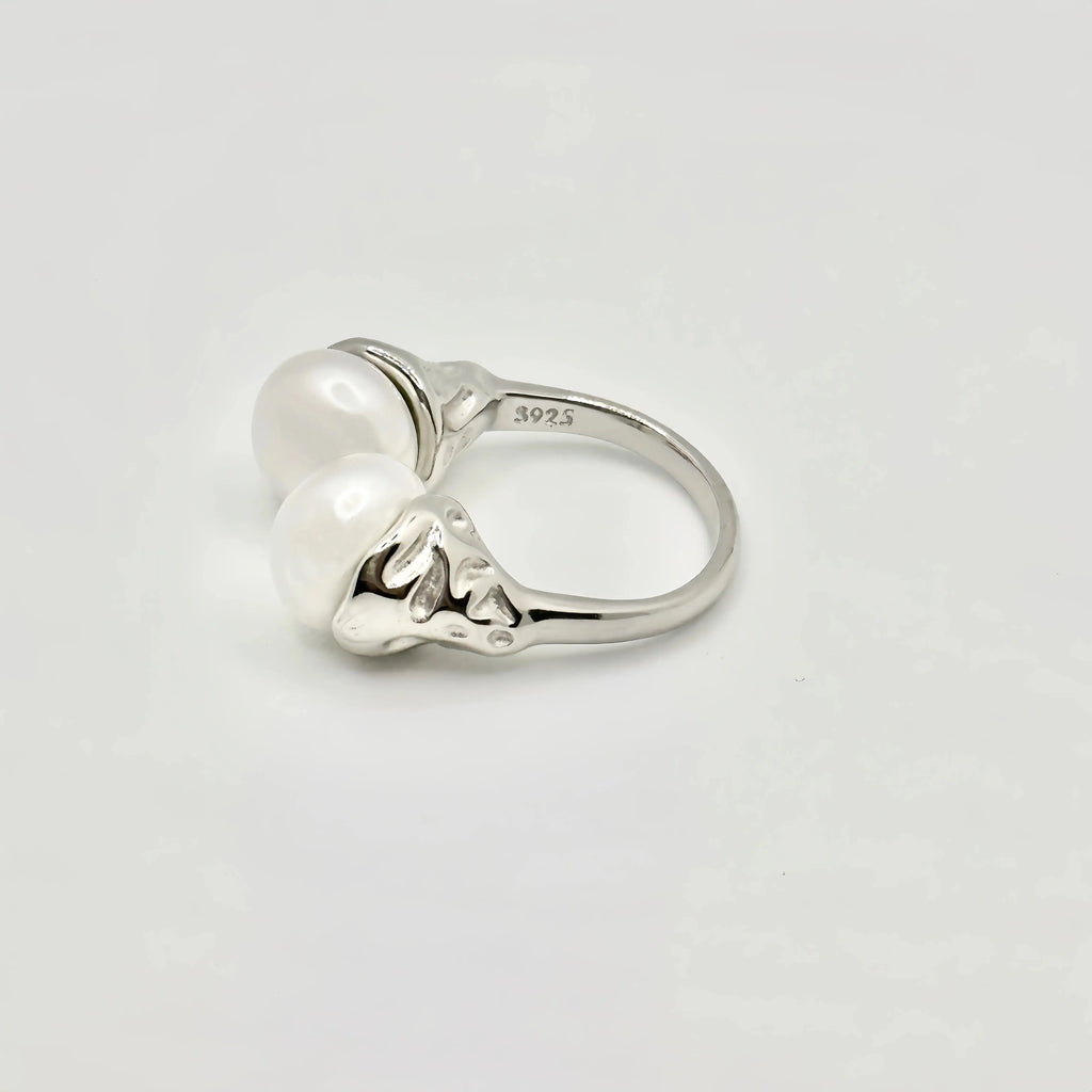 A unique sterling silver ring marked 'S925' indicating its purity, featuring a split-shank design that holds two large, lustrous pearls. The metal between the pearls is crafted to resemble a stylized floral or heart pattern, adding a decorative touch to the piece.