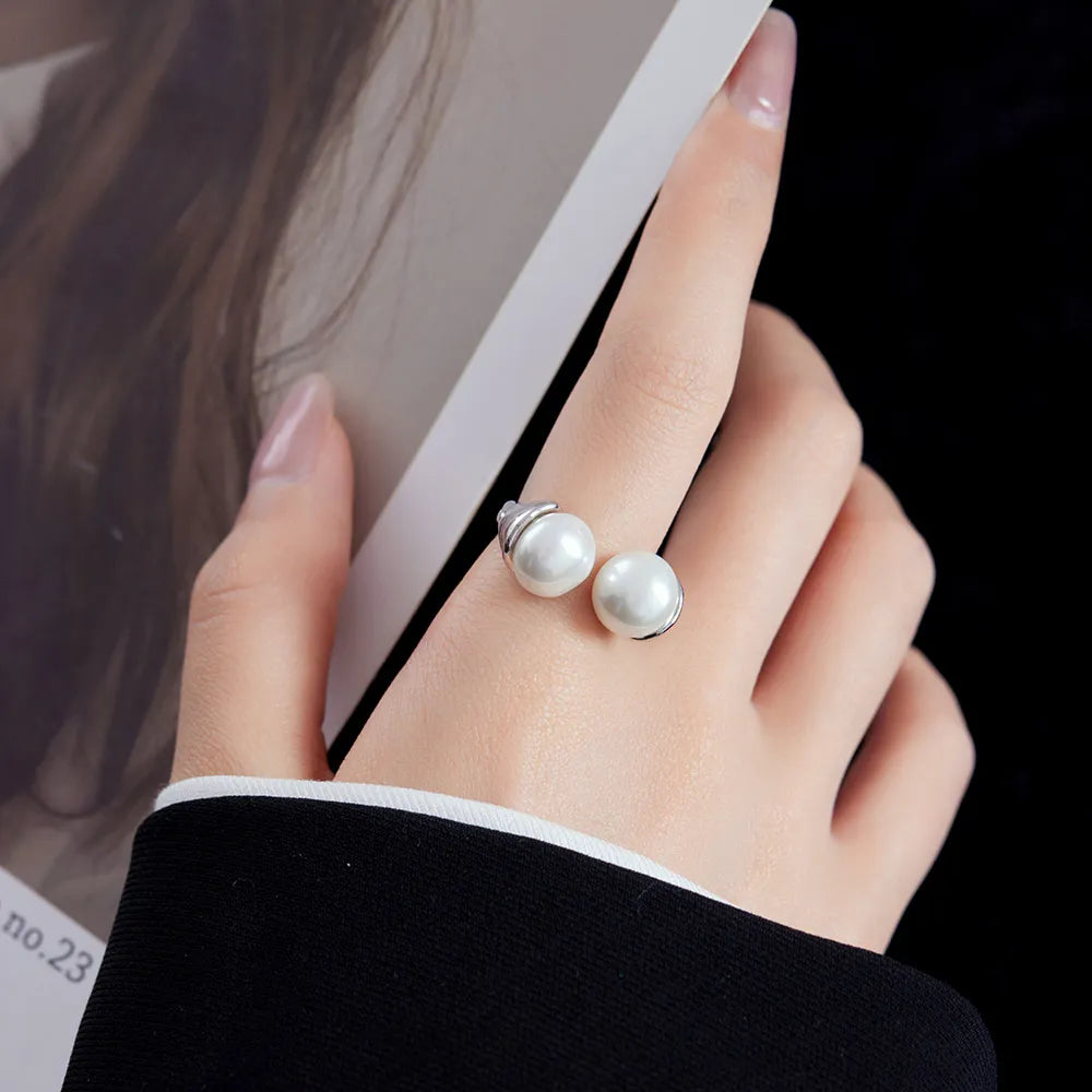 A unique sterling silver ring marked 'S925' indicating its purity, featuring a split-shank design that holds two large, lustrous pearls. The metal between the pearls is crafted to resemble a stylized floral or heart pattern, adding a decorative touch to the piece.