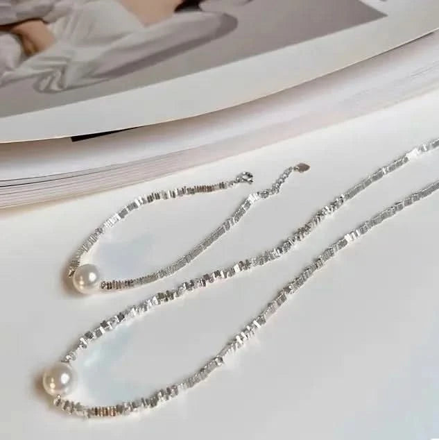 A woman wearing a silk top is adorned with a delicate choker-style necklace, composed of small shimmering beads with a single prominent pearl centered gracefully along her collarbone. The necklace exudes subtle sophistication and highlights the gentle curve of her neck.