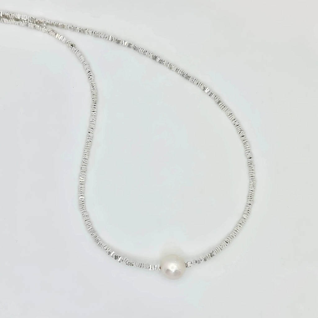 A simple and elegant silver necklace with a thin, flexible chain that leads to a single large pearl at its center. The design is minimalist, focusing on the lustrous beauty of the pearl, which is the standout feature of this classic piece of jewelry.