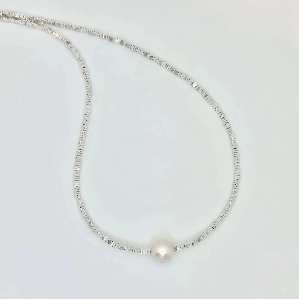 A simple and elegant silver necklace with a thin, flexible chain that leads to a single large pearl at its center. The design is minimalist, focusing on the lustrous beauty of the pearl, which is the standout feature of this classic piece of jewelry.