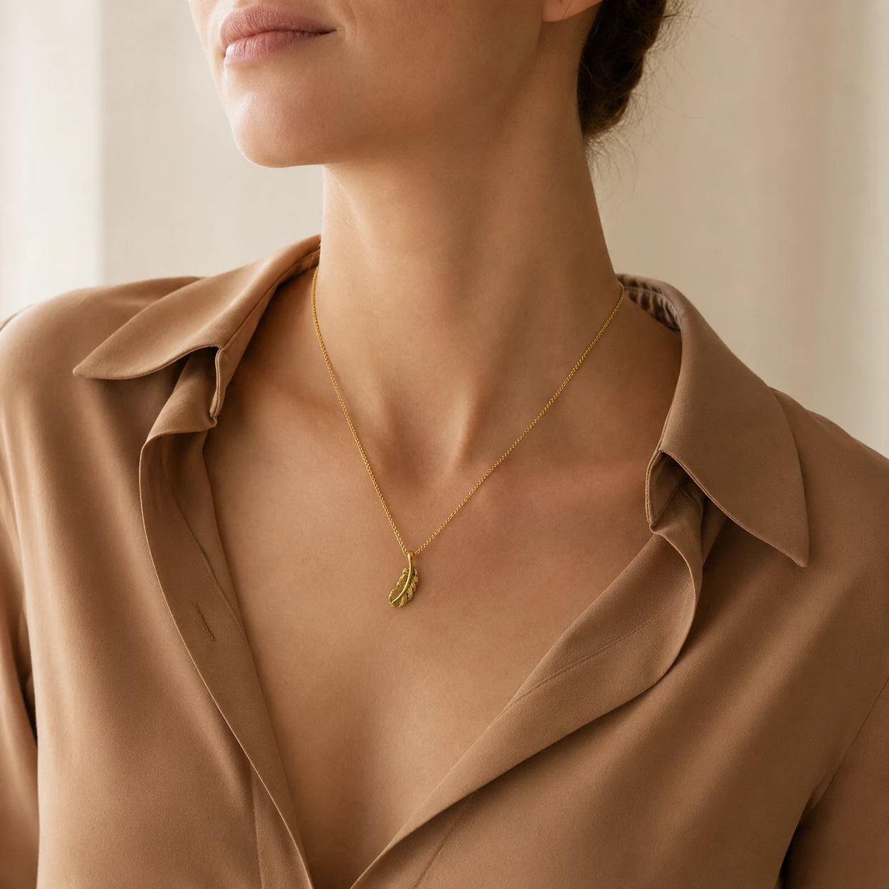 Model wearing gold-tone sterling silver feather pendant necklace