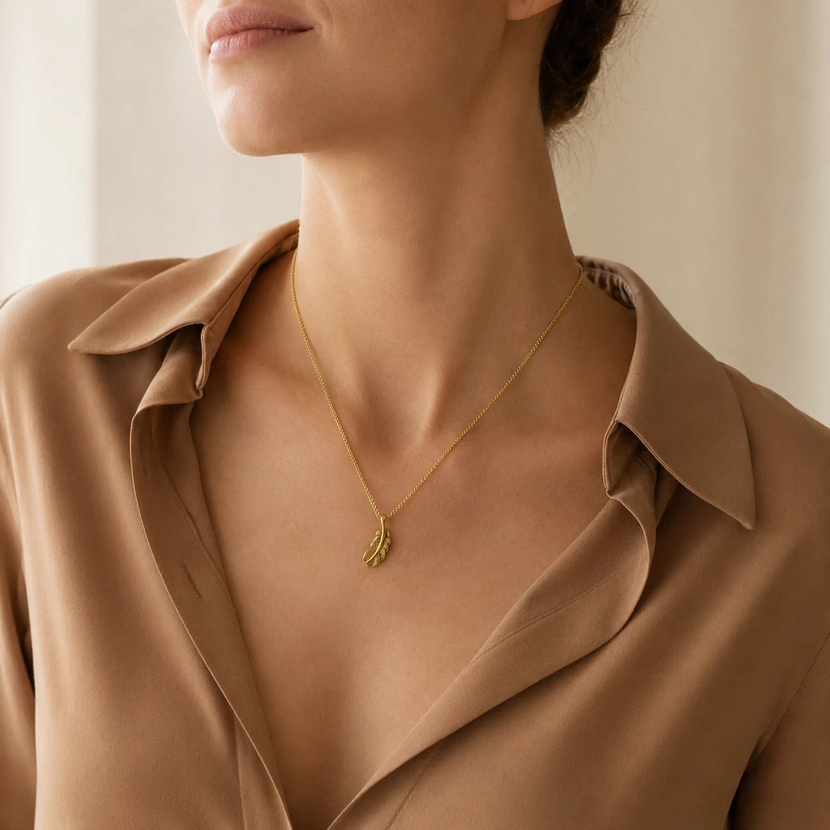 Model wearing gold-tone sterling silver feather pendant necklace