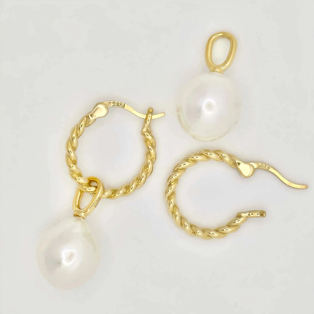 This image features a pair of gold earrings, each adorned with a large, lustrous white pearl. The pearls exhibit a smooth, round shape with a glossy finish, appearing well-matched in size. The metallic components of the earrings are gold in color, suggesting high-quality metal, possibly gold, crafted in a simple yet elegant twisted chain design. The background is a muted, light color, accentuating the jewelry's color and sheen.