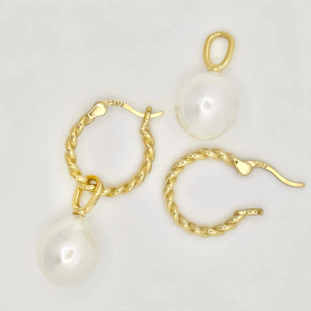 This image features a pair of gold earrings, each adorned with a large, lustrous white pearl. The pearls exhibit a smooth, round shape with a glossy finish, appearing well-matched in size. The metallic components of the earrings are gold in color, suggesting high-quality metal, possibly gold, crafted in a simple yet elegant twisted chain design. The background is a muted, light color, accentuating the jewelry's color and sheen.