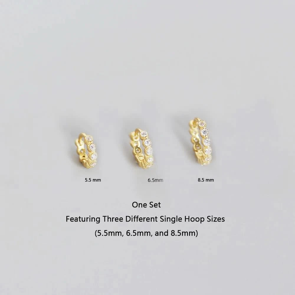 Three gold hoop earrings of different sizes on a gray background