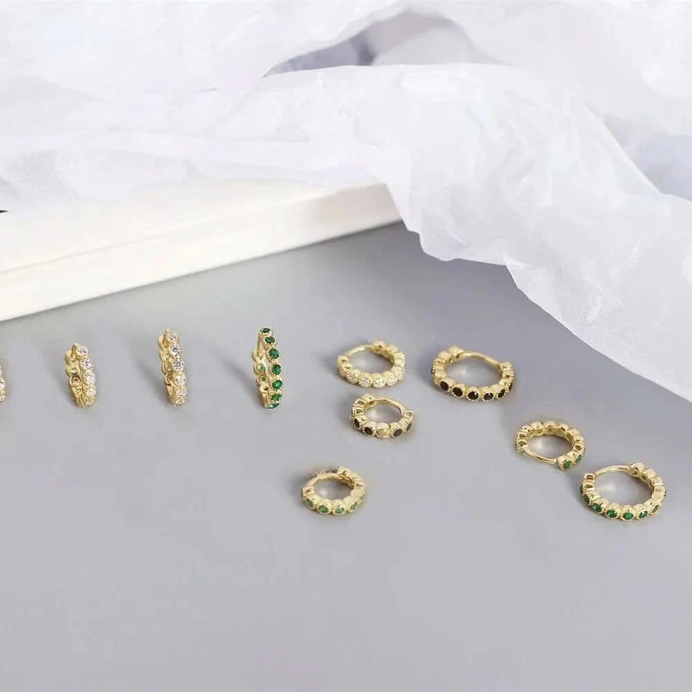 Gold hoop earrings with green gemstones on a gray surface