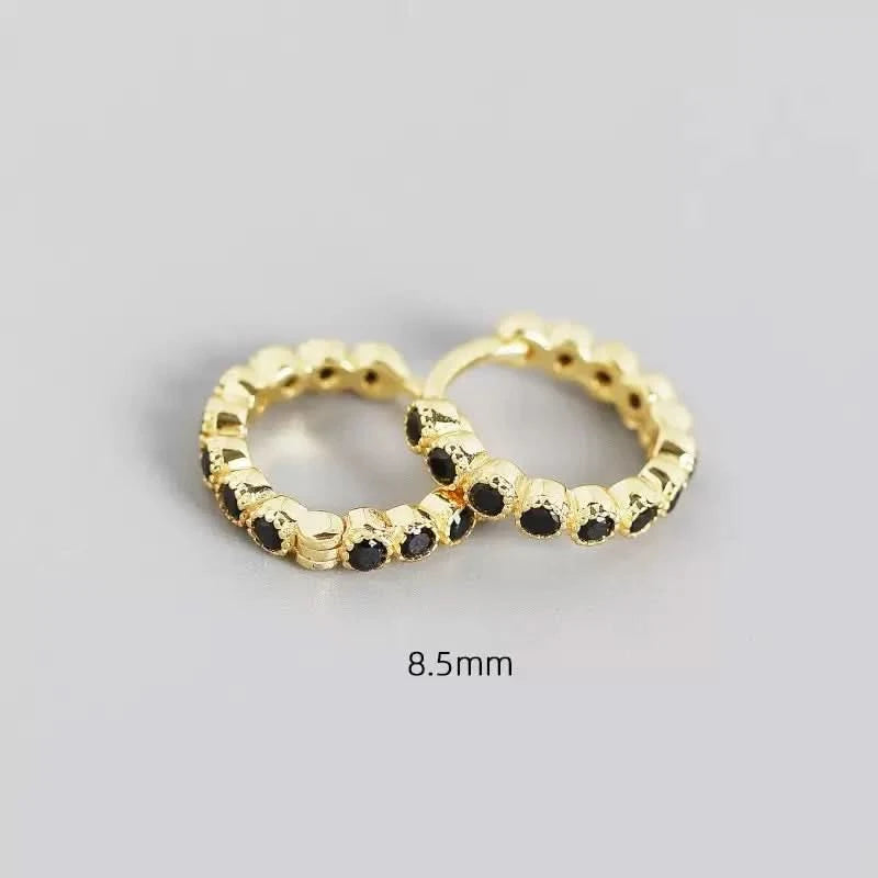 Pair of gold hoop earrings with black stones on a gray background