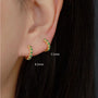 Gold hoop earrings with green gemstones worn by a person, shown close-up with measurements.