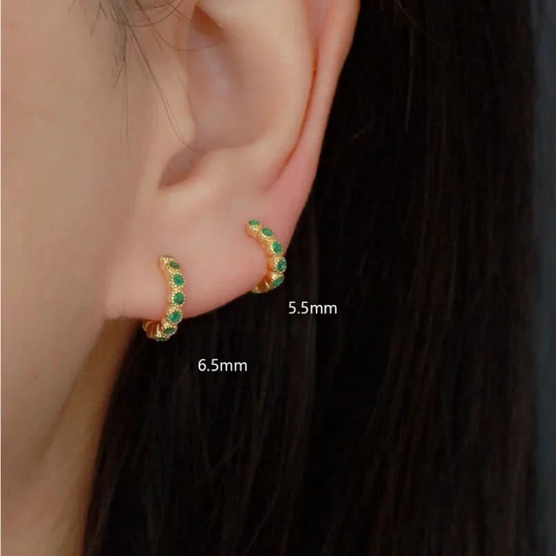 Gold hoop earrings with green gemstones worn by a person, shown close-up with measurements.