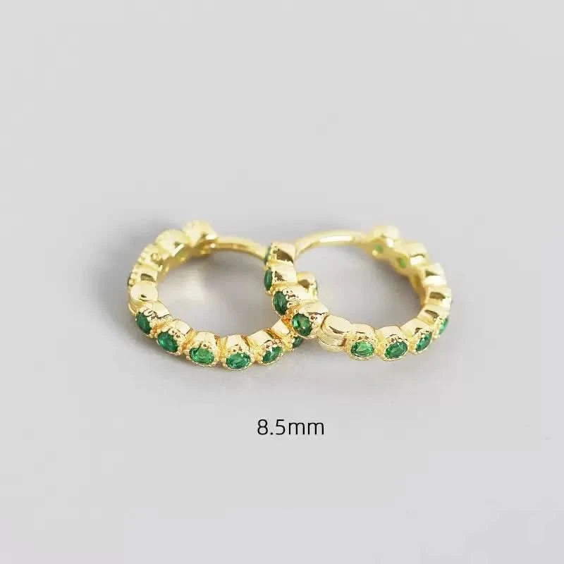 Gold hoop earrings with green gemstones on a gray background