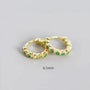 Gold hoop earrings with green gemstones on a gray background