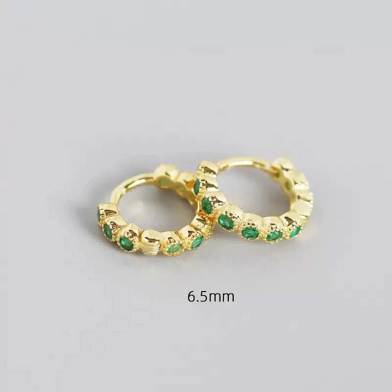 Gold hoop earrings with green gemstones on a gray background