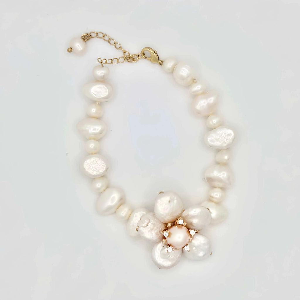 A gold brooch with a floral design, featuring large, baroque pearls as petals, a smaller central pearl, and golden balls accentuating the center and edges. The lustrous pearls have a natural, irregular shape, which adds to the unique and organic feel of the piece, set against a white background.