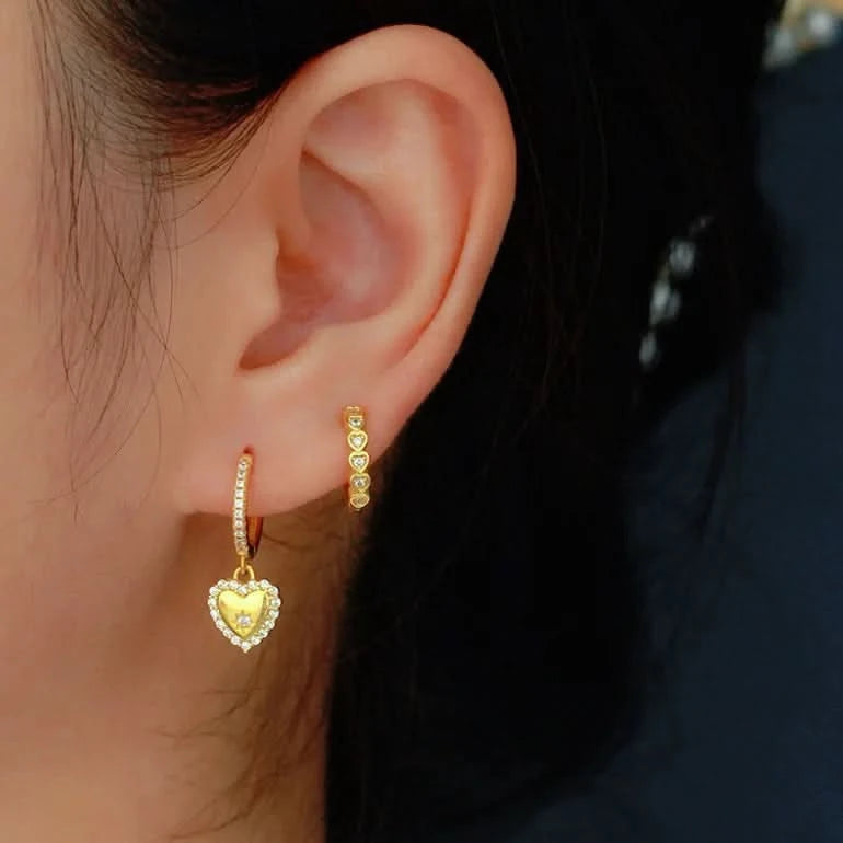 Close-up of an ear wearing gold heart-shaped hoop earrings with a blurred background