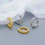 Two pairs of gold and silver hoop earrings on a light gray background.