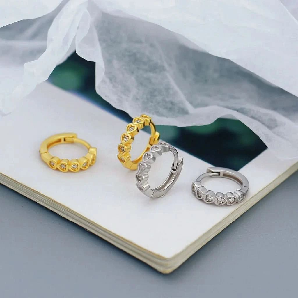 Four gold and silver hoop earrings on a white surface with a gray background