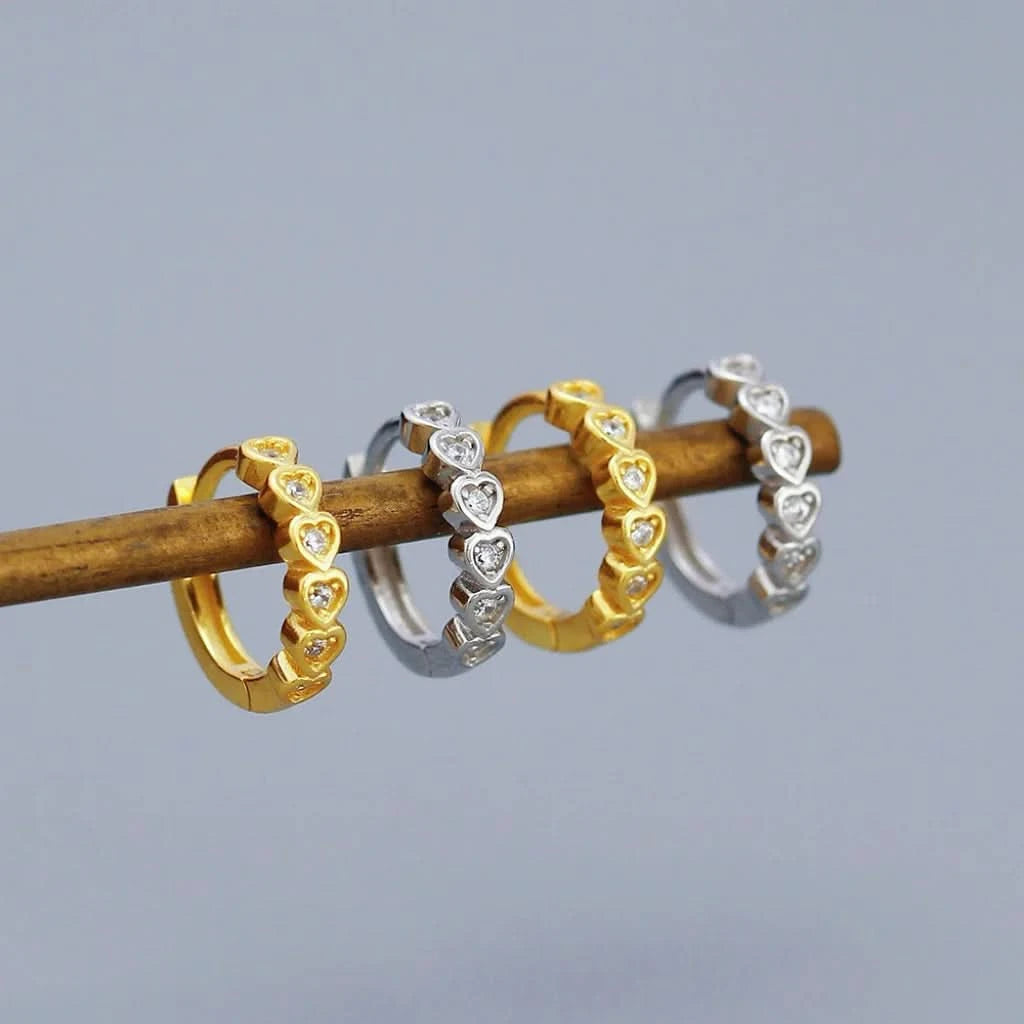 Three heart-shaped ring sets in gold, silver, and rose gold on a wooden stick against a gray background.