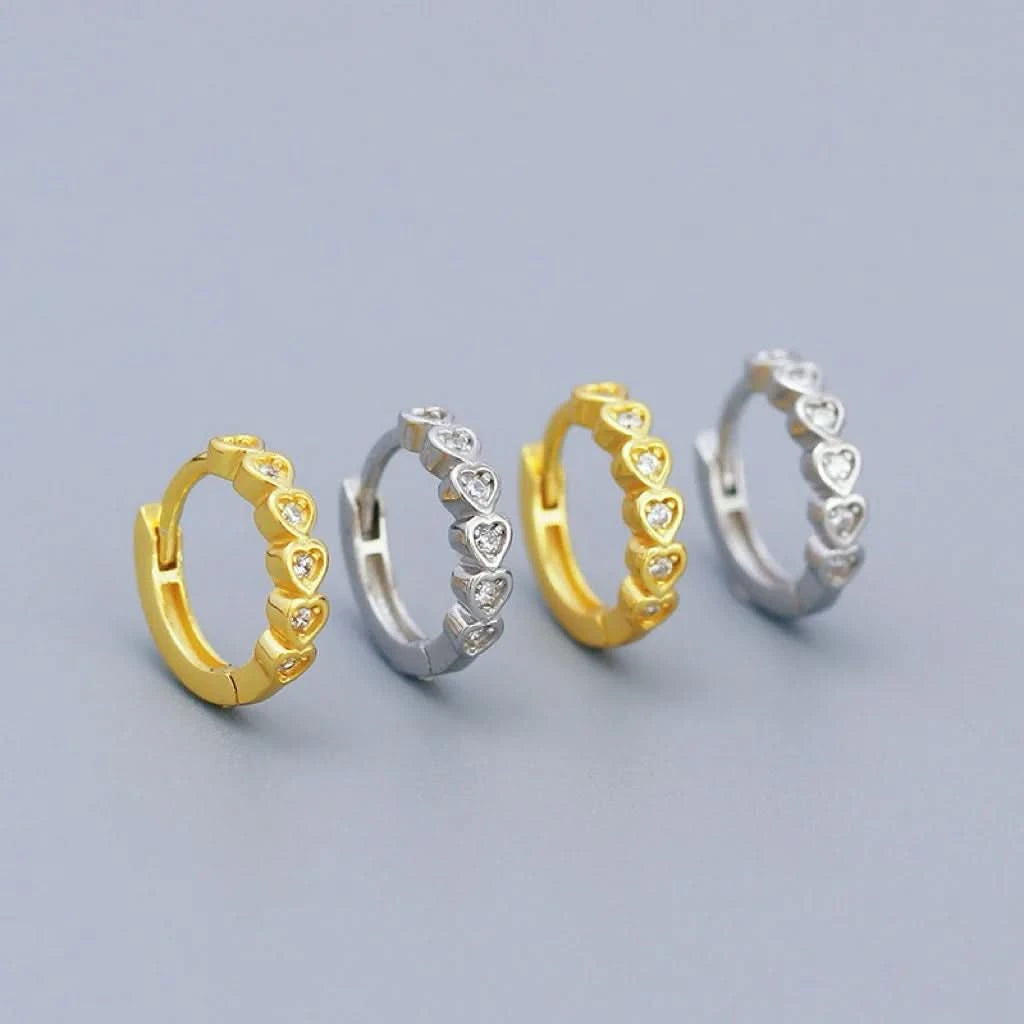 Four heart-shaped hoop earrings in gold and silver on a light gray background