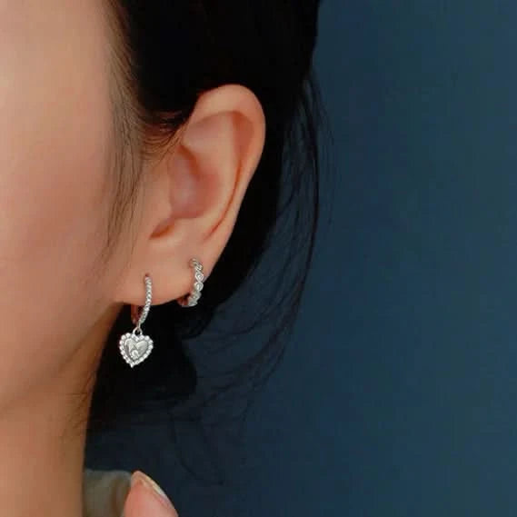 Close-up of a person wearing silver heart-shaped earrings against a dark background