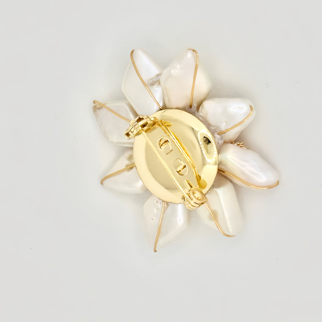 The image depicts a gold-toned hair clip with a large, star-shaped design crafted from iridescent baroque pearls. At the center is a detailed pink rose, encircled by a gold chain loop. Adjacent to the rose is a single, dark green gemstone, adding a contrasting pop of color. The overall design suggests a blend of natural elegance and ornate detailing, presented against a clear, neutral background.