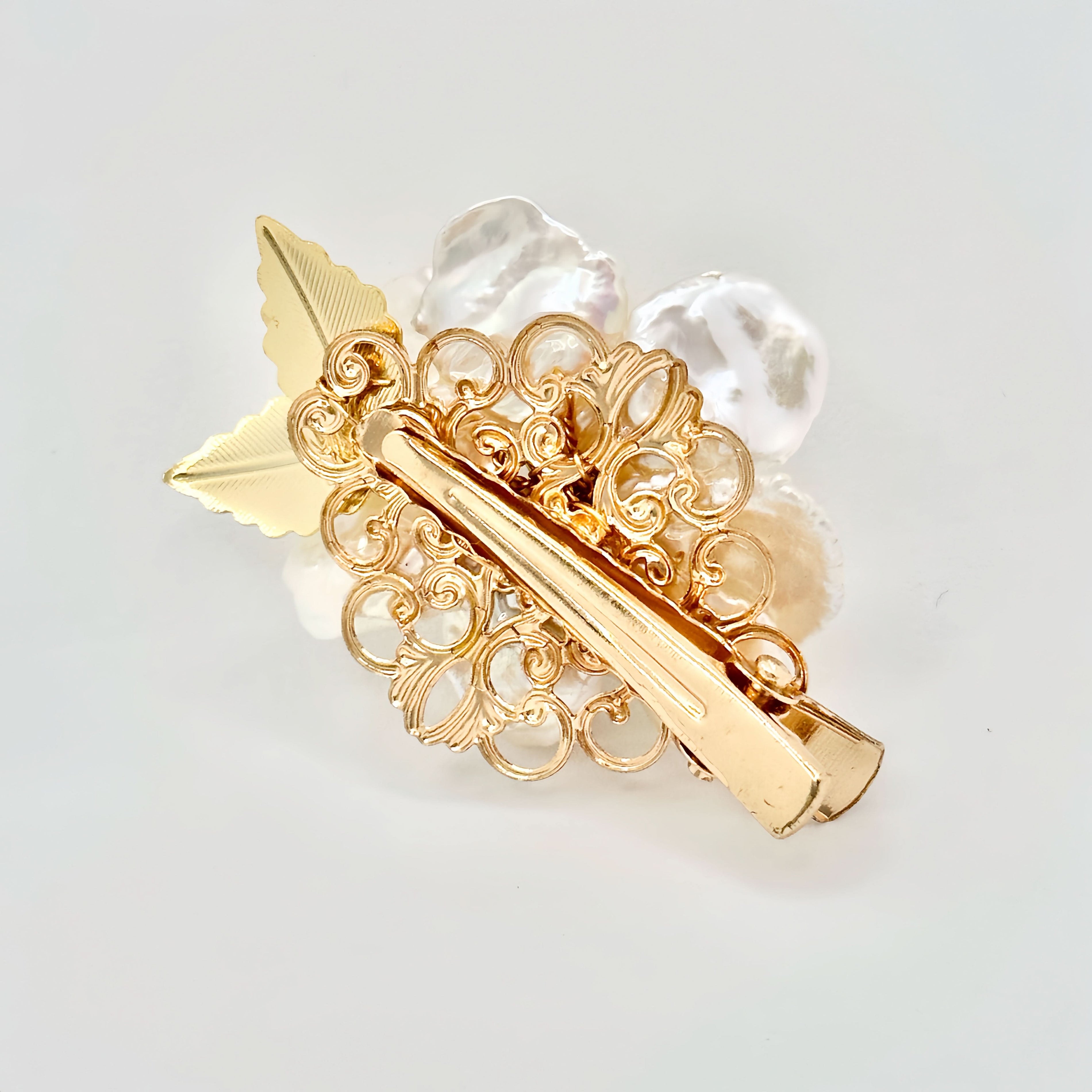 Gold hair clip with a pearl flower design, green jade center, and sparkling accents on a light background.