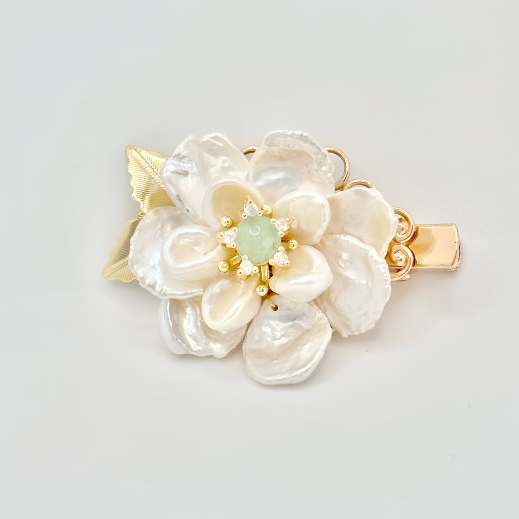 Gold hair clip with a pearl flower design, green jade center, and sparkling accents on a light background.