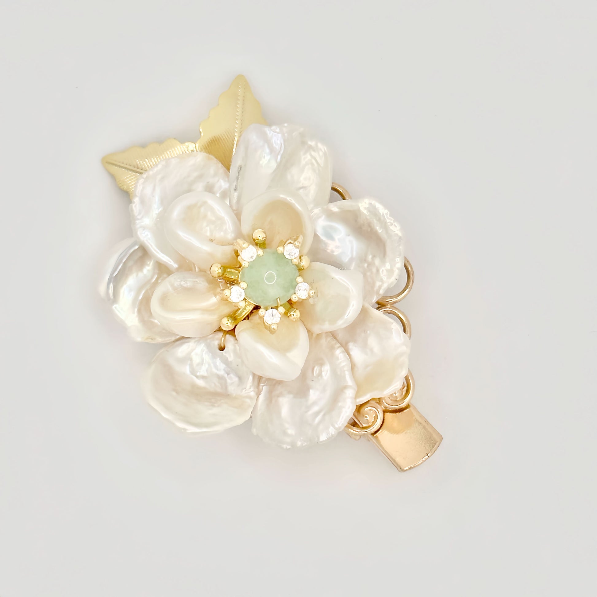 Gold hair clip with a pearl flower design, green jade center, and sparkling accents on a light background.