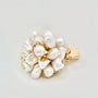 The image showcases a luxurious gold hair clip with a floral motif, featuring a central round pearl surrounded by an array of baroque pearls forming petals. Each pearl petal is edged with tiny gold accents, adding a hint of sparkle. The overall design captures the essence of an opulent blossom, with the golden tones warmly complementing the creamy luster of the pearls. The clip's background is a clean, solid color that accentuates the jewelry's elegant details.