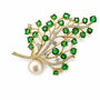 Green crystal branch brooch with clear crystals, pearl accent and gold-tone setting on a white background