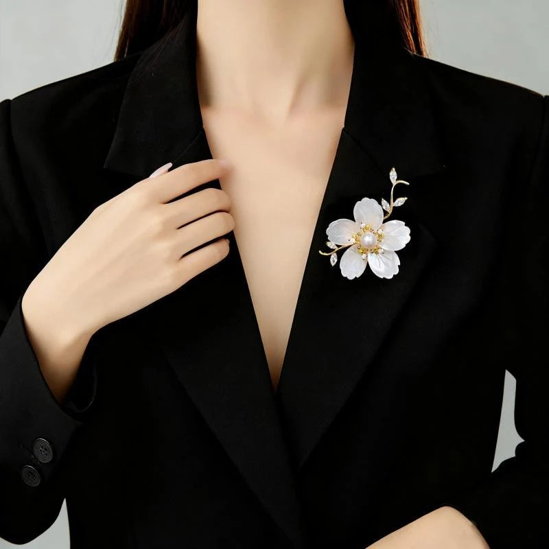 Mother-of-pearl flower brooch with pearl centre worn on a black blazer lapel