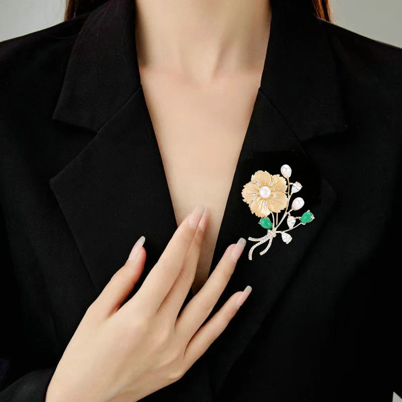 Close-up of gold floral bouquet brooch with carved mother-of-pearl petals, pearl buds and green stones on a blazer