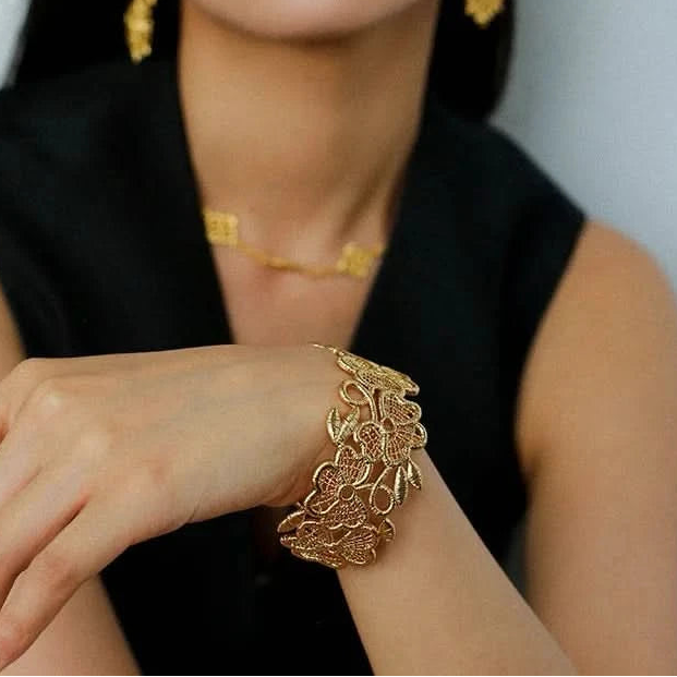 Woman wearing gold jewelry including earrings, necklace, and bracelet against a neutral background