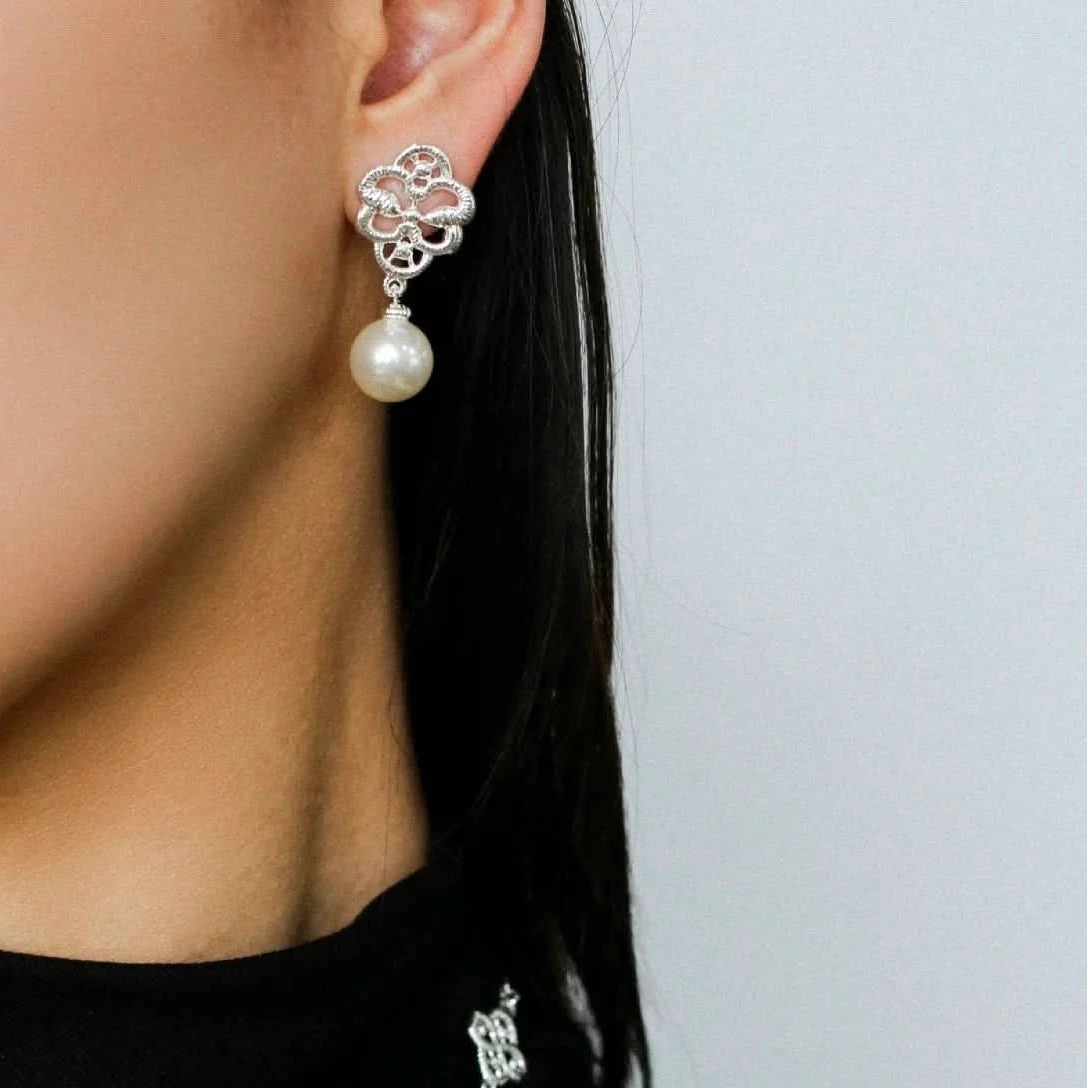 Close-up of a person wearing silver earrings and a matching necklace against a plain background