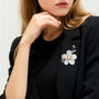 Close-up of mother-of-pearl flower brooch with gold-tone crystal branch detail on a black blazer