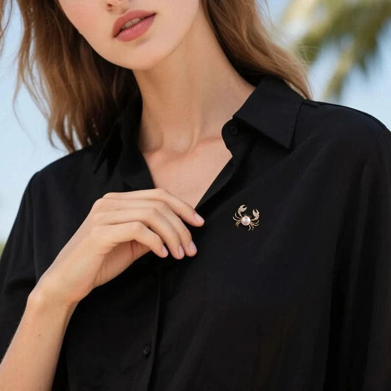 Gold-tone pearl crab brooch with cubic zirconia claws worn on a black blouse