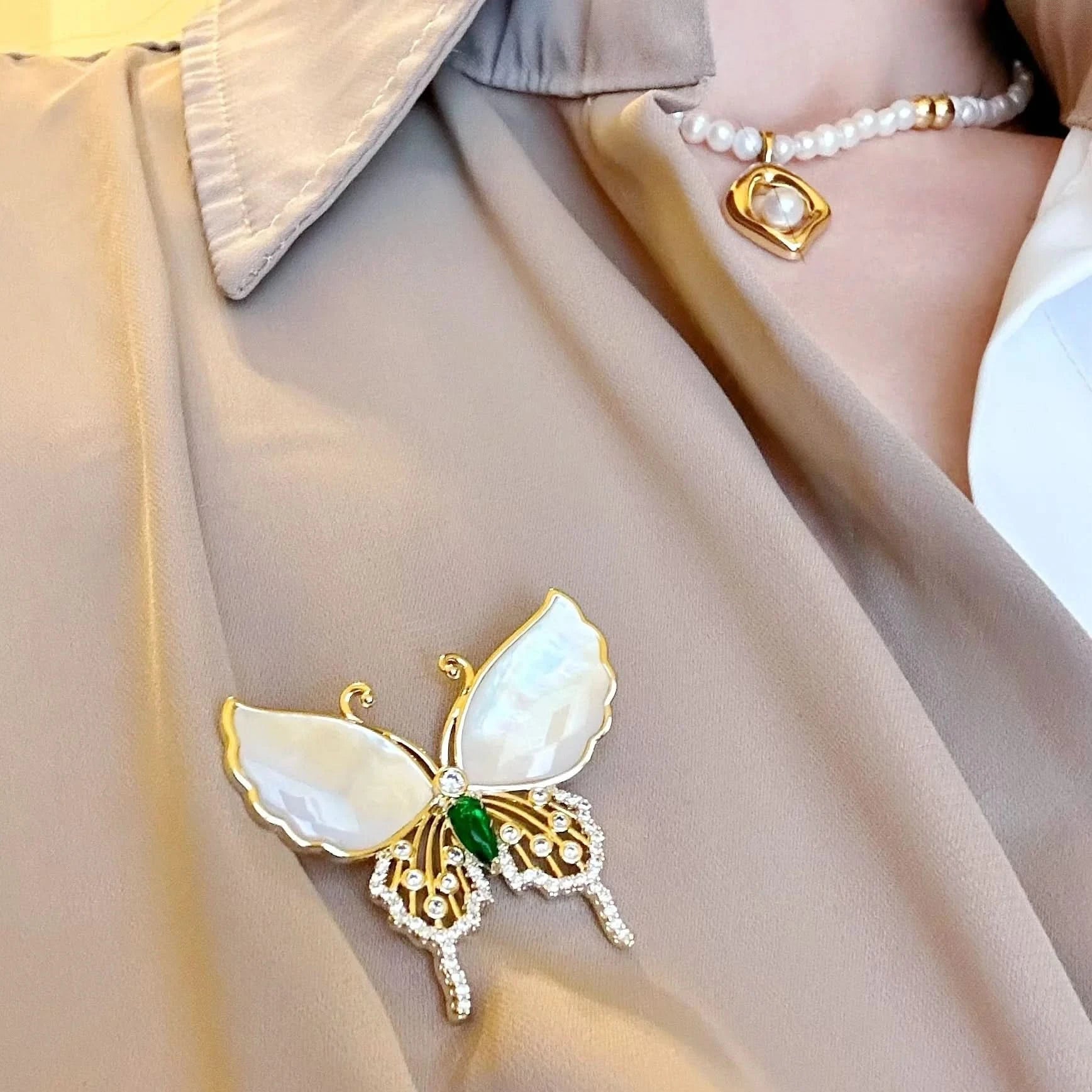 Butterfly-shaped brooch with gold and green accents on a beige garment.