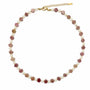 Carved rhodochrosite flower and white stone beaded necklace with gold-tone details on a white background