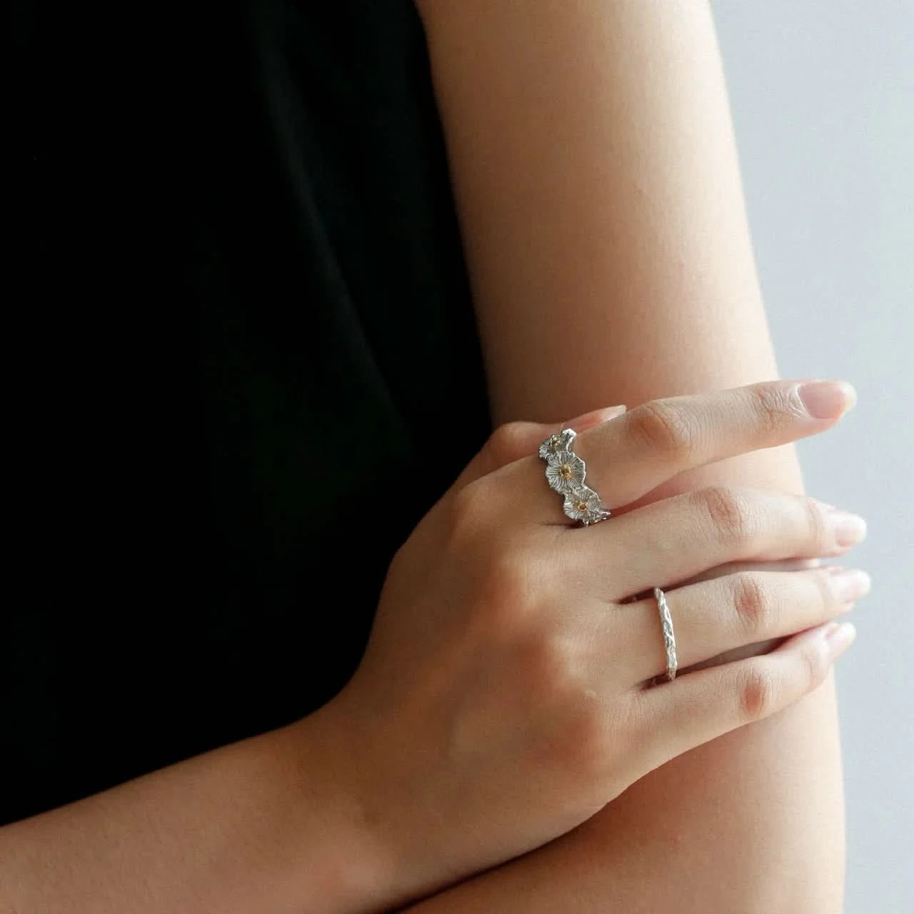 Close-up of a hand wearing two silver rings with floral designs 