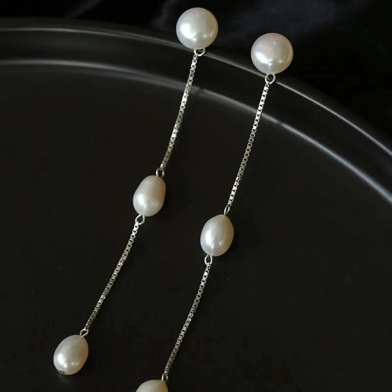 Pearl earrings with silver chains on a dark background