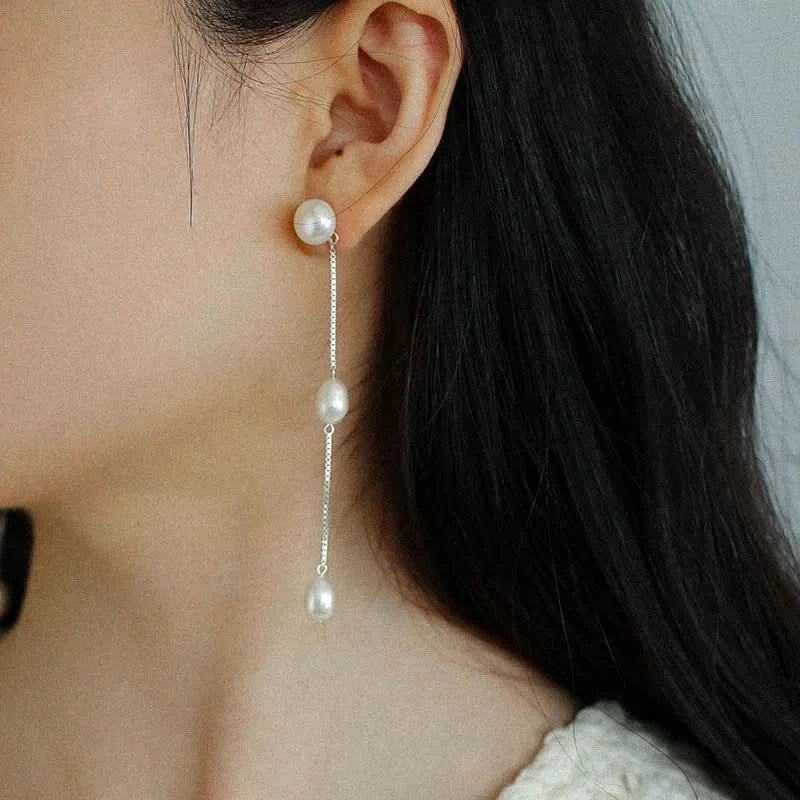 Pearl earring with chain on an ear against a neutral background