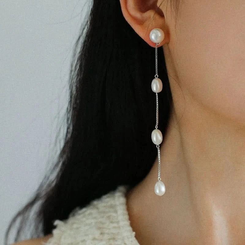 Pearl drop earrings worn by a person with a neutral background
