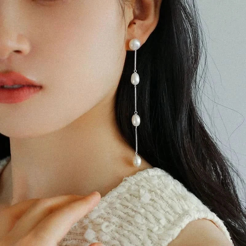 Close-up of a person wearing pearl drop earrings with a neutral background
