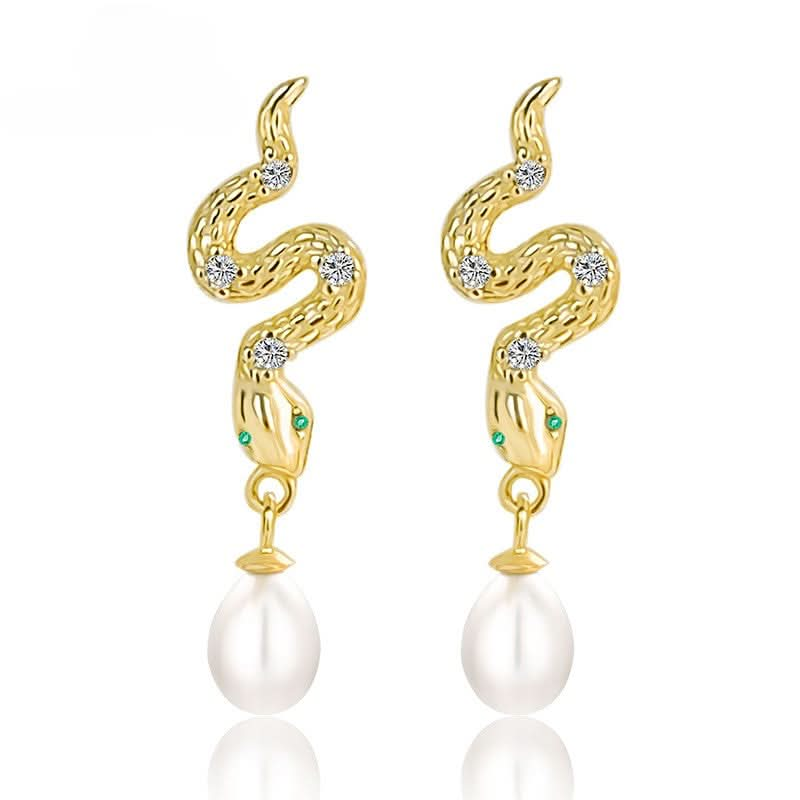 A pair of elegant gold-plated snake earrings, each featuring a sinuous design with textured scales. The snakes are embellished with small diamonds set along their bodies and tiny green crystals for eyes. Each earring is completed with a dangling white pearl at the bottom, adding a classic and sophisticated finish to the piece.