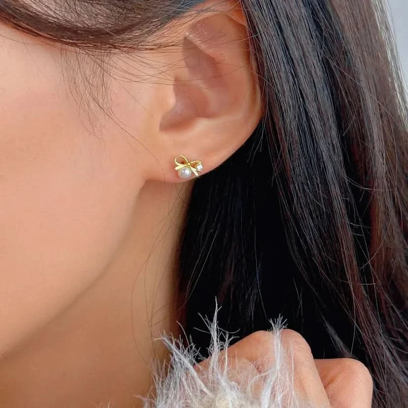 Close-up of a person wearing a gold bow-shaped earring with pearl center.