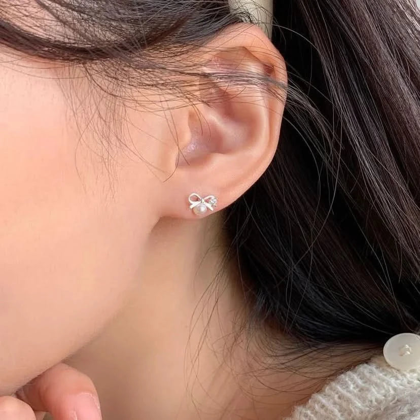 Close-up of an ear wearing a bow-shaped earring with a pearl center.