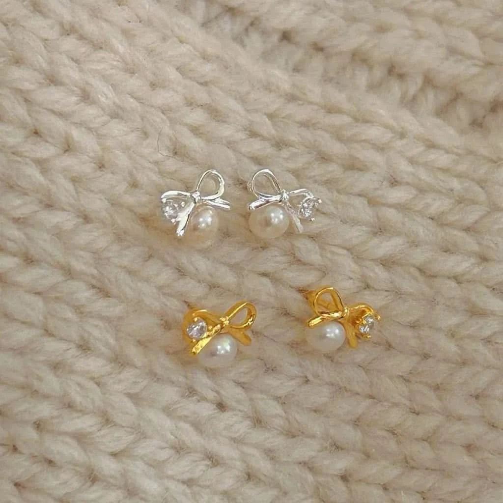 Pair of pearl earrings with gold and silver bows on a beige knitted fabric background