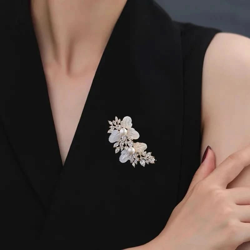 White floral crystal brooch with pearl accents worn on a black blazer lapel