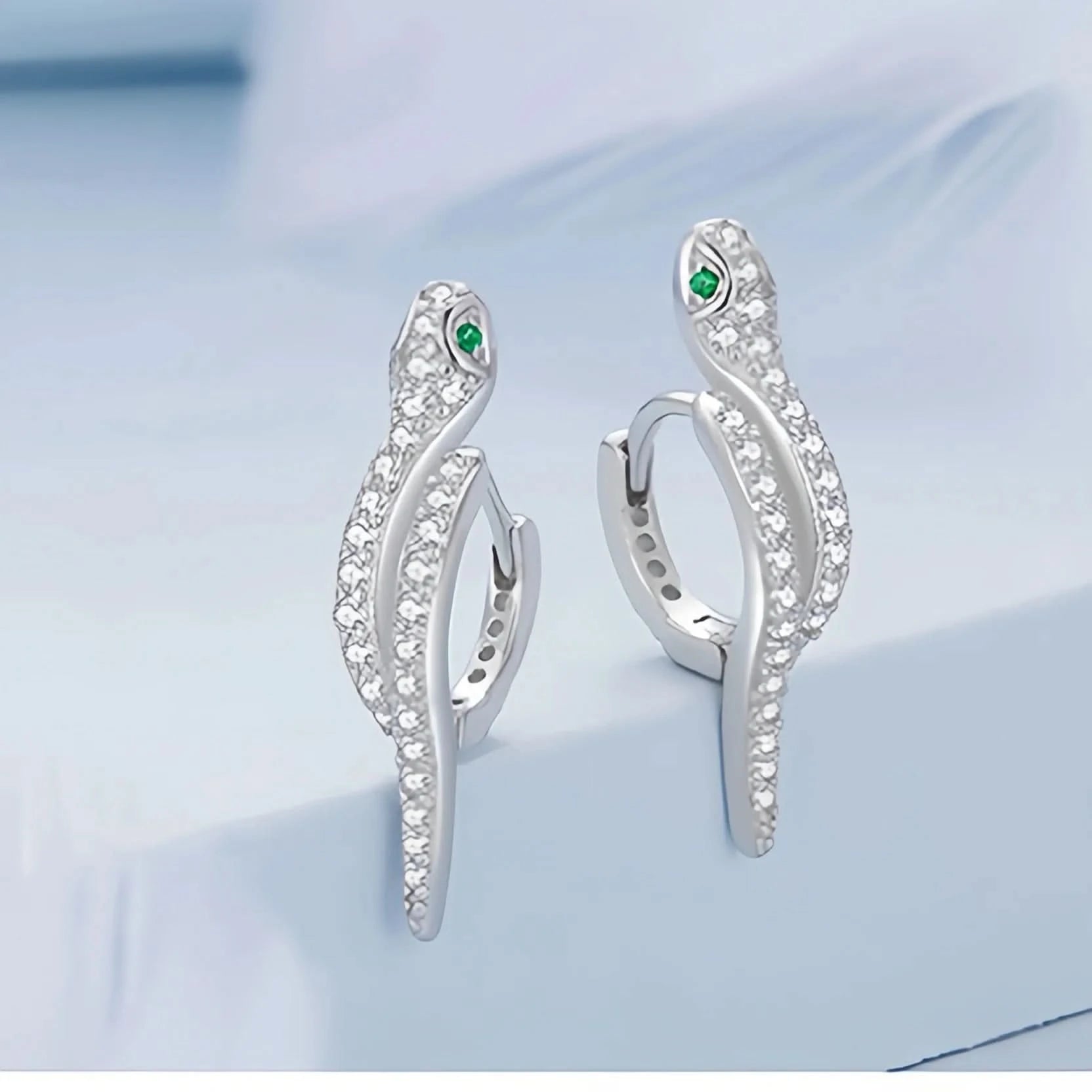 An elegant silver ring designed to resemble a serpent, adorned with numerous small crystals along its body. The snake's head is detailed with a pair of green crystal eyes, and the ring is stamped with 'S925' to indicate sterling silver purity.